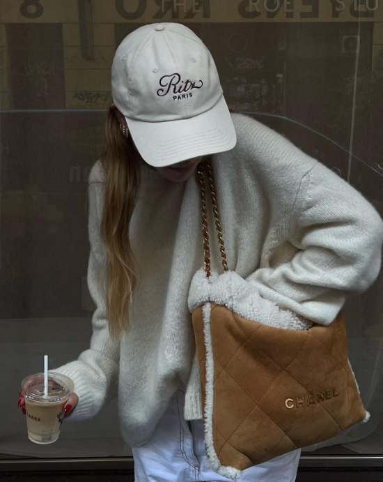 Girl wearing a shearling chanel 22 bag with a ritz frame hat on and drinking a iced coffee