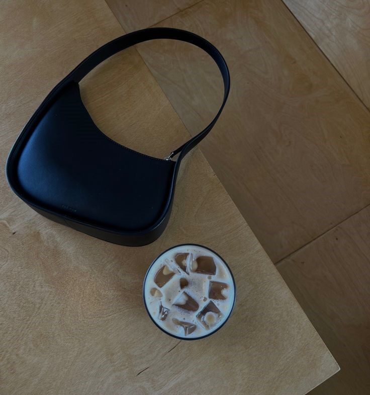 black leather the row half moon bag with ice coffee laying on a table
